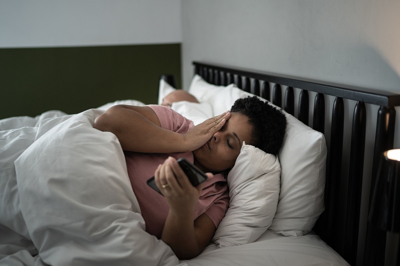 Woman laying in bed in the morning, checking her phone, looking tired.