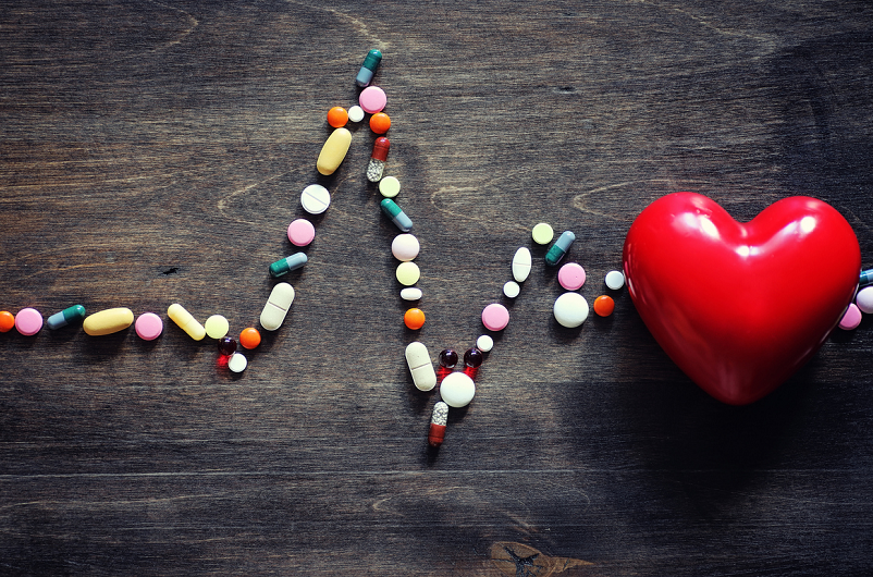 Heart supplement pills on a wooden countertop, with a red heart.