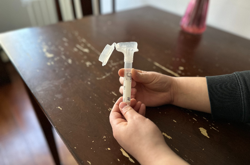 A close up of a woman's hands holding a tube for saliva collection for cancer genetic testing.