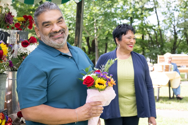 Carlos Mercado holding a bouquet of flowers smiling.