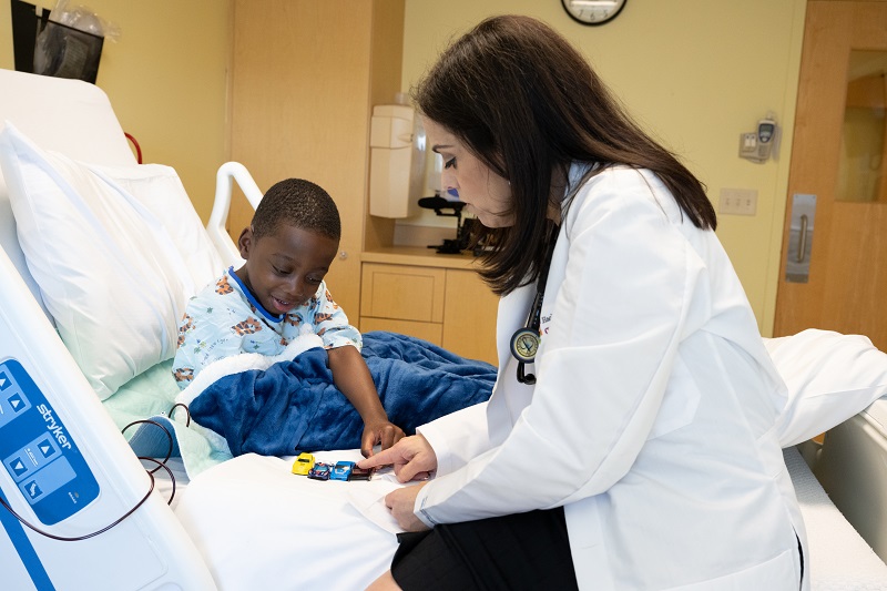 Stacey Rifkin-Zenenberg, D.O. and patient Tobi playing with toy cars on his patient bed.