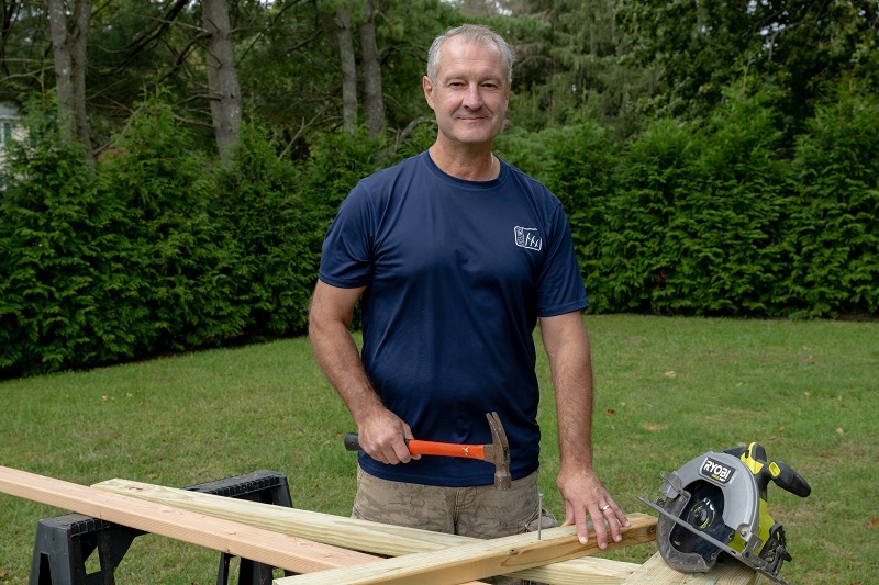 John Sherrod smiling and wood working outside.