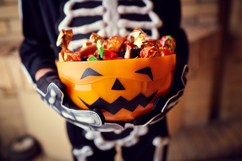 kid in skeleton costume holding bowl of halloween candy
