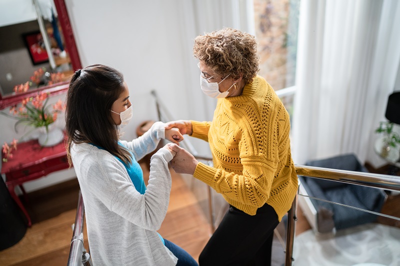 Young woman helping an older woman walking down stairs, holding hands. Older woman is suffering from Parkinson's disease.