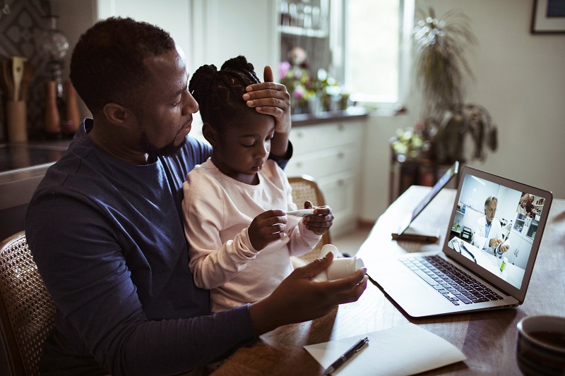 Father sits with daughter who is sick while on conference call with physician. Cold flu or RSV