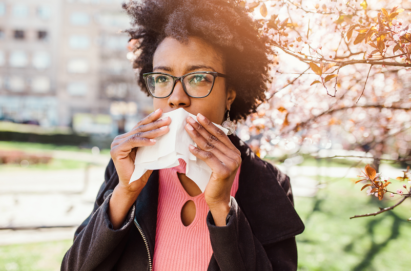 Woman blowing her nose in the park, feeling the affects of allergies