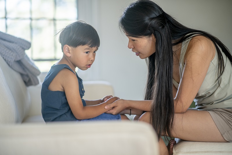 Mother speaks closely with her son as he sits on the couch, helping him process his emotions.