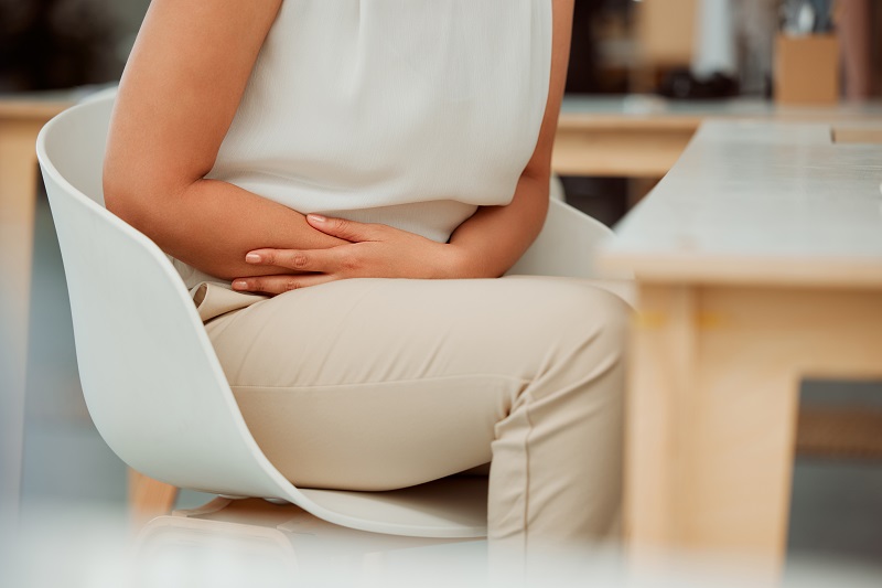 Close up of a woman dressed in business attire, clenching her stomach from pains, or a UTI.