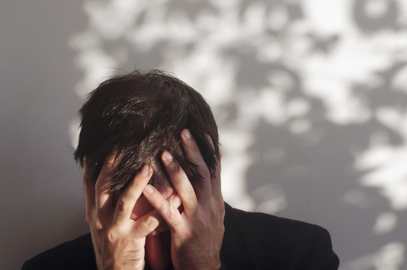 Man stressed with his hands over his face, leaning forward. Dealing with substance use disorder