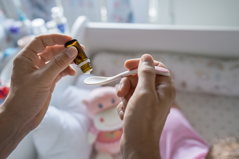 Close up of a father's hands preparing spoon with probiotic drops medicine for his baby