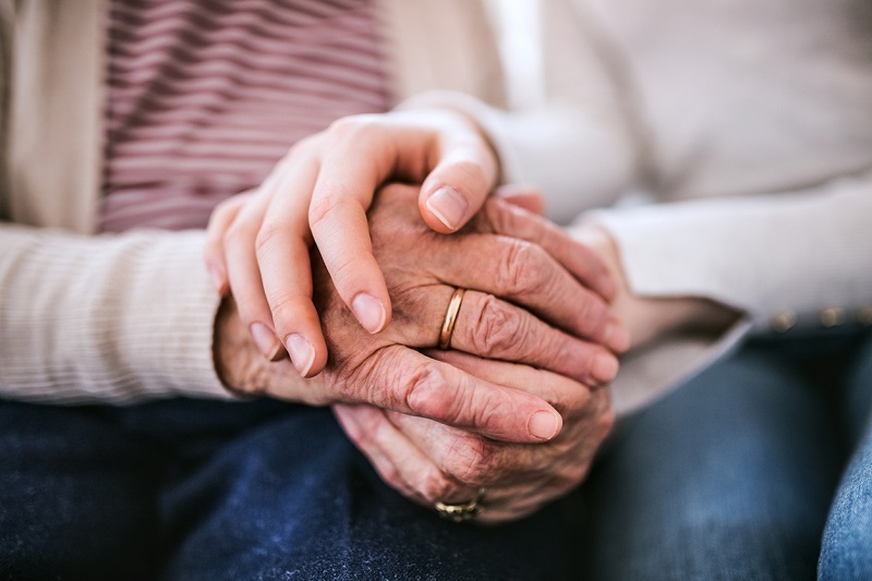 ounger caregiver holding the hands of an elderly loved one. Alzheimer's disease concept.