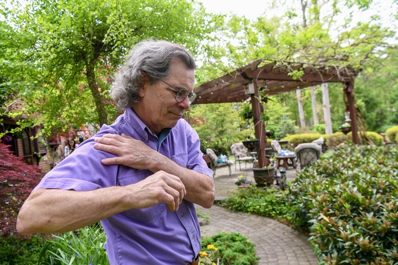 Man outside, holding his shoulder in pain while lifting his arm up.