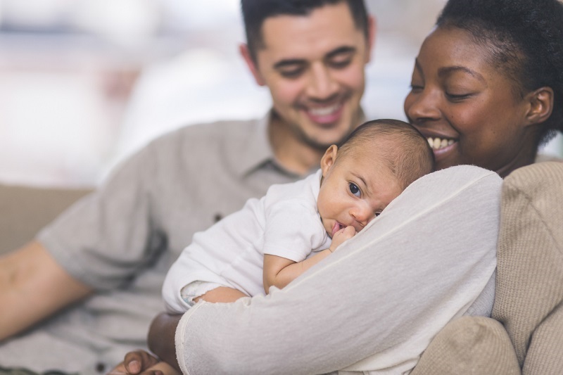 New mom holds her baby to her chest, with dad sitting close by on the couch.