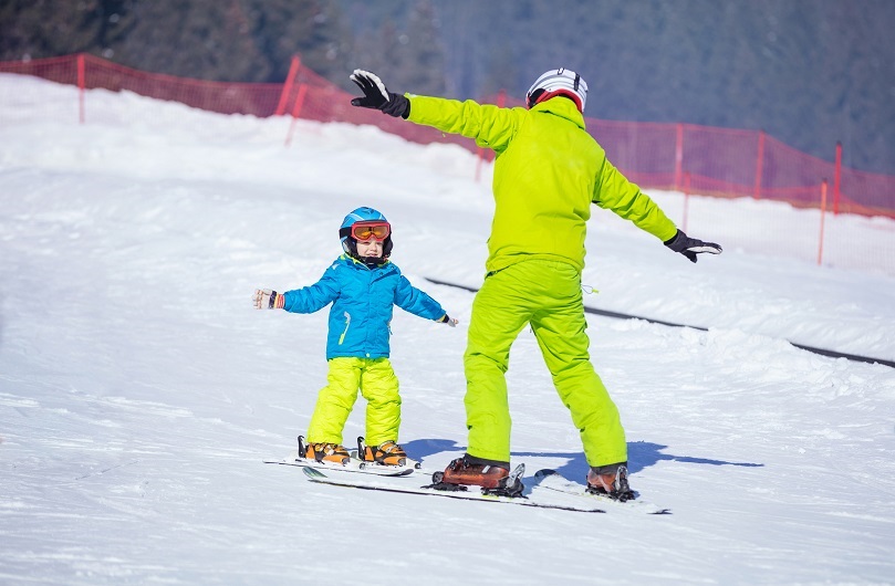 Instructor teaching little skier how to make turns, young boy doing exercise on slope in children's area.