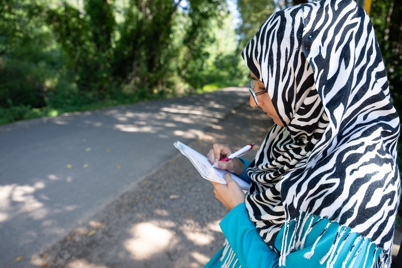 Woman writing in a notebook, standing outside. Journaling concept.