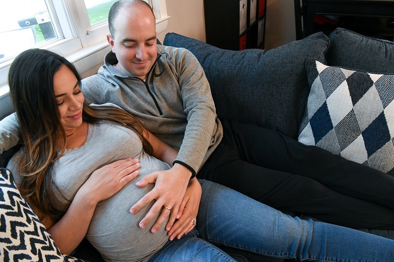 Husband and pregnant wife sitting on the couch smiling and feeling the baby move, with hands on her belly.