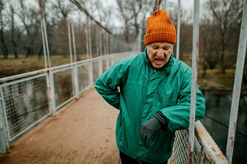 An older man, resting on a bridge while out of breath.