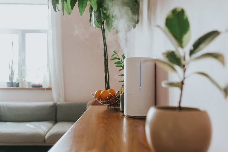 A humidifier releasing steam on a counter space in a living room.