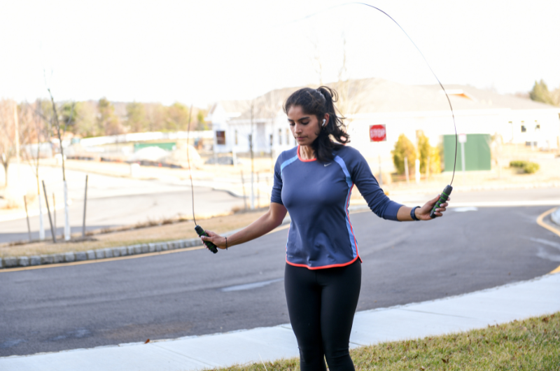 Young woman exercises by jumping rope outdoors.
