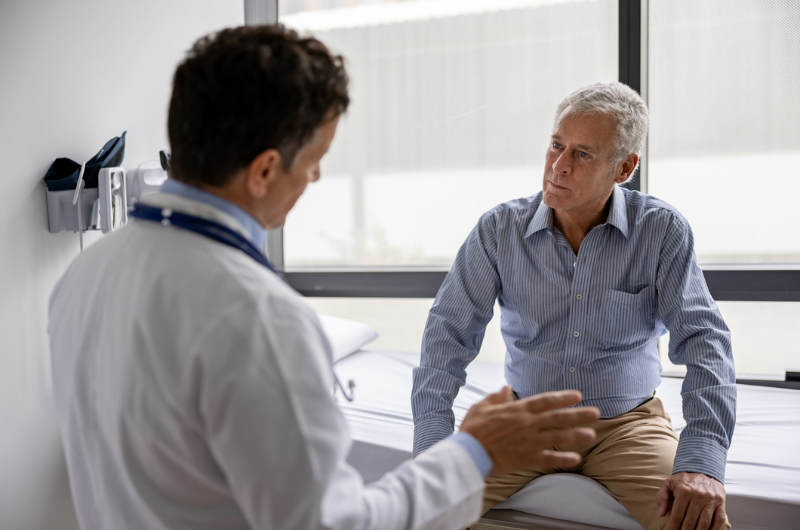 An older man sits and listens as his doctor explains colonoscopy prep.