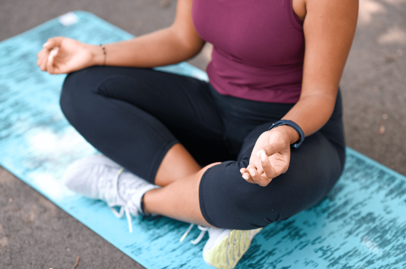 A woman sits cross-legged on the ground as she meditates.