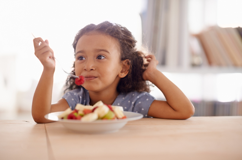 Brunette little girl eating fruit salad at a table.
