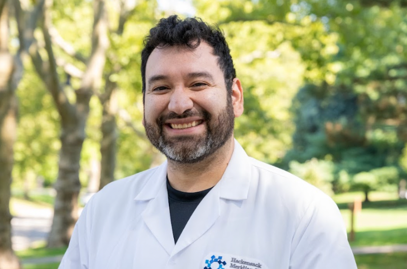 Standing outdoors, family medicine specialist Kevin Vasquez, M.D., smiles at the camera with greenery behind him.