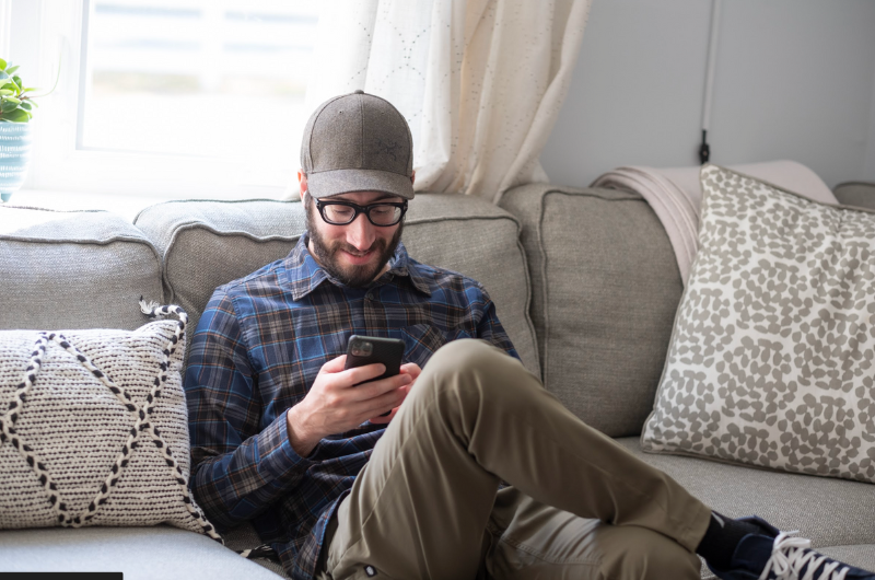 Young man sits on a sofa while texting on his smartphone.
