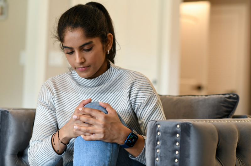 Young woman clutches her knee while sitting down.