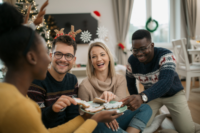 Diverse group of friends eating Christmas themed cookies and smiling.