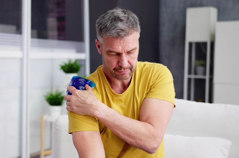 Middle-aged man applies a cool gel pack to his shoulder.