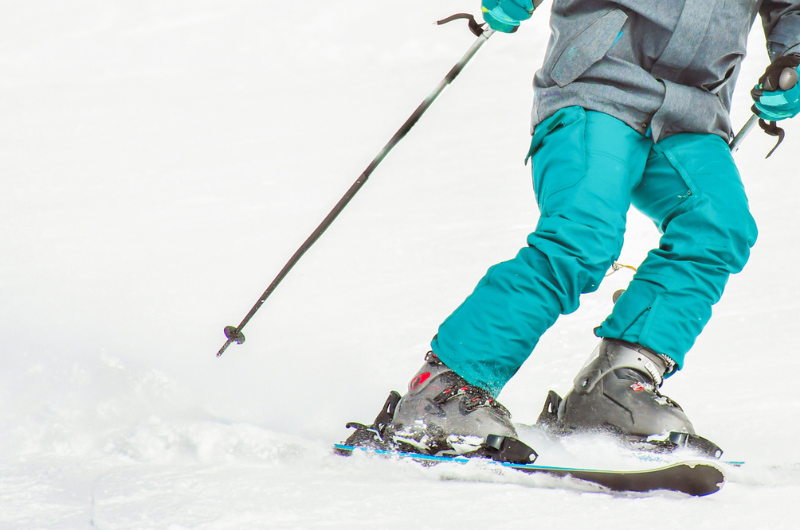 Close up of blue pants and poles of skier going downhill.