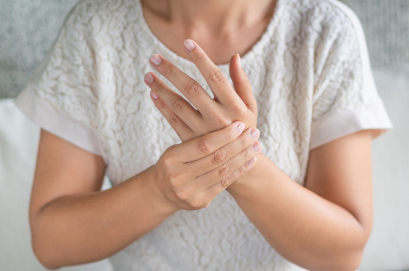 Close-up of a young woman sitting on sofa dealing with a numb hand.