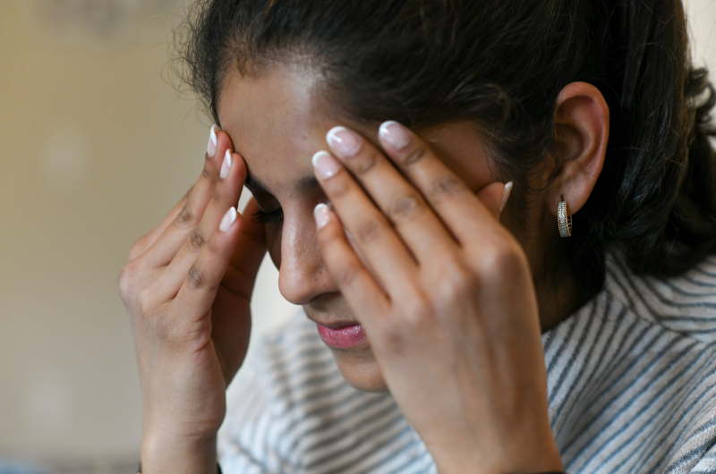 A young woman holds her hands to her head in pain.