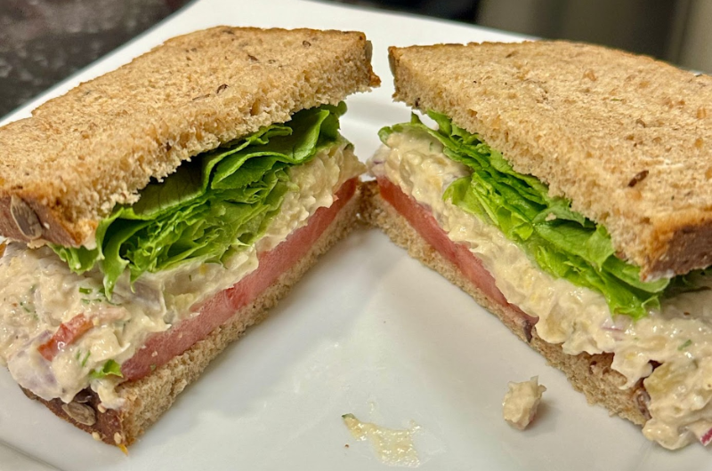 A chickpea “tuna” salad sandwich on wheat bread, sliced in half.