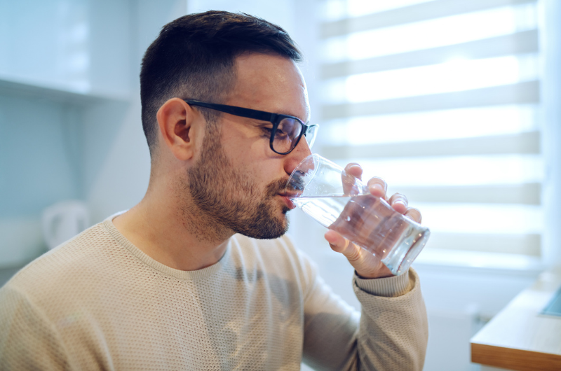 Side view of a Caucasian man sitting at a dining table drinking a glass of water.