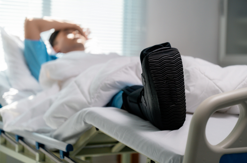 Patient wearing a walking boot lying in a hospital bed while recovering from bunion surgery.