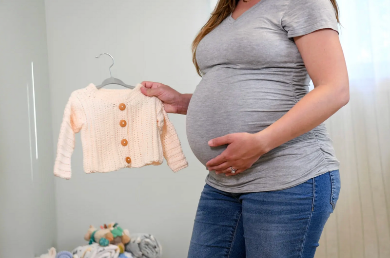 A pregnant woman holding a small sweater and touching her belly.