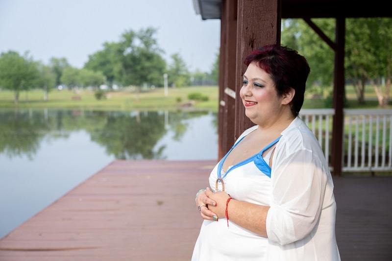Woman stands on a dock looking out at the water smiling.