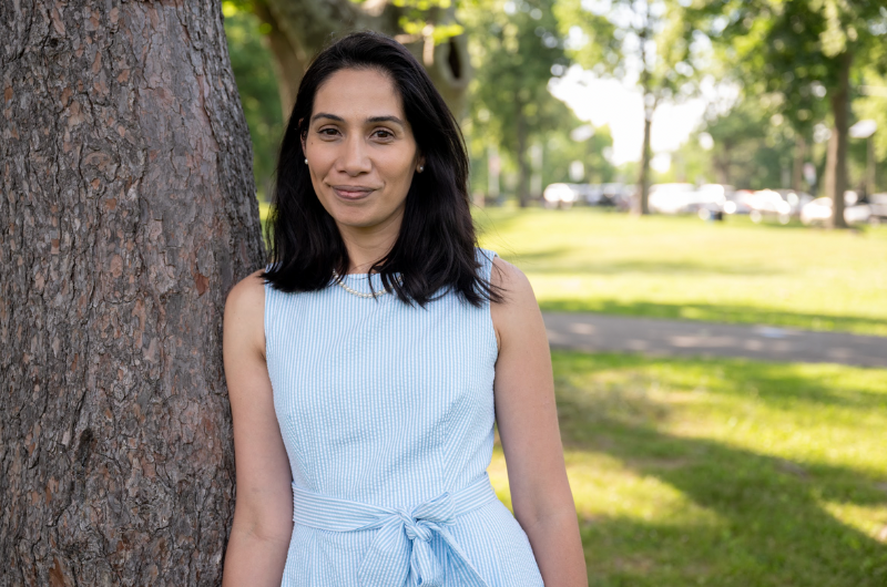 Woman smiling, leaning against tree in the park.