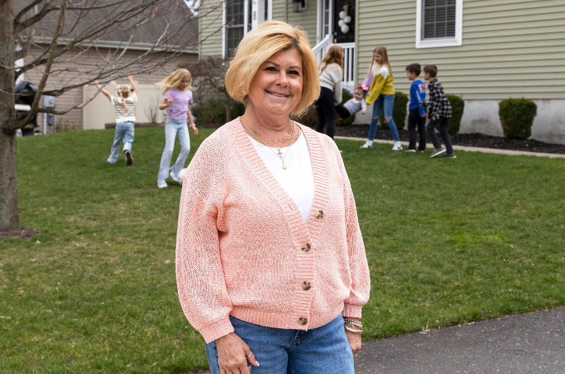 Geralyn Fogarty, now 67, stands in her front yard as her grandchildren play in the background.