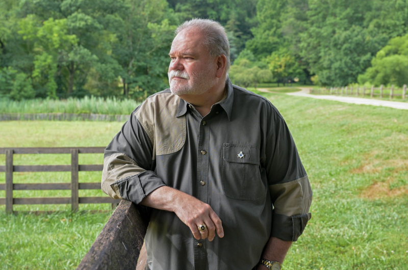 Don Dudley looks off into the distance as he leans against a wooden fence.