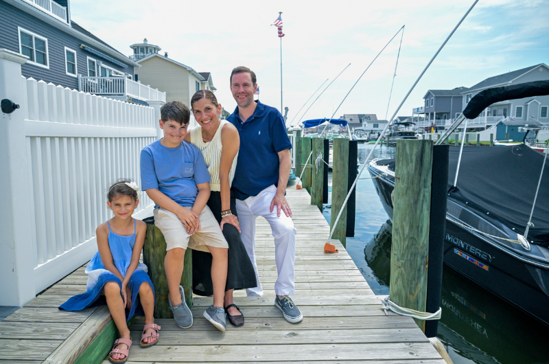 45-year-old Eva Maravelias sits on a dock next to a boathouse with her son, daughter and husband.