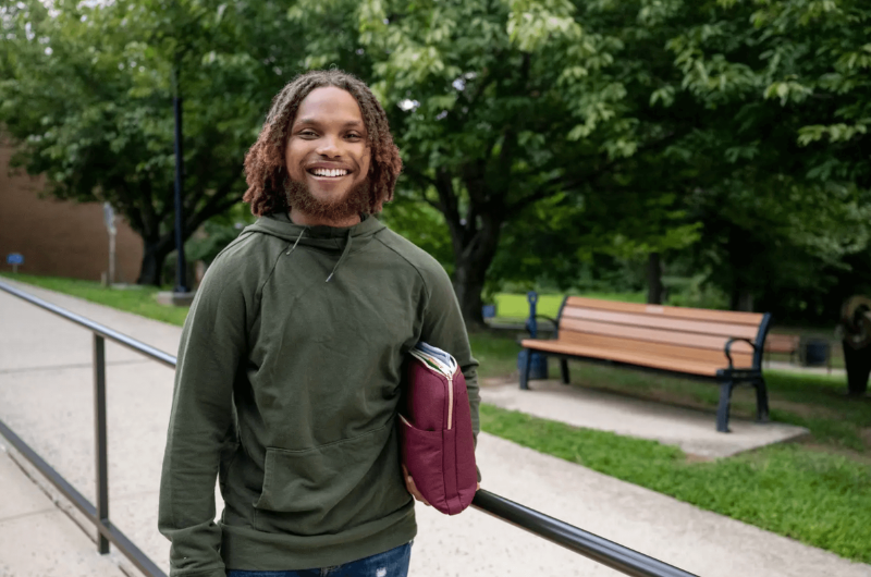 Wearing a forest green hoodie, 21-year-old Thomas Pender smiles at the camera.