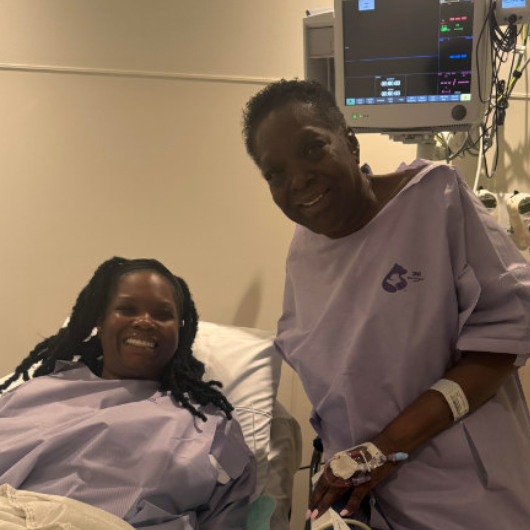 Curlean Phillips stands next to her daughter, who is in a hospital bed.