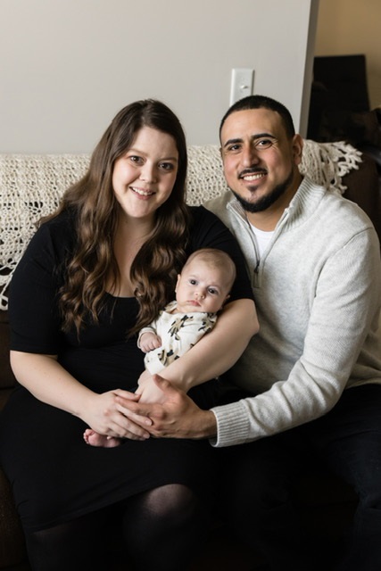 Baby Benny being held by his parents, all smiling, sitting on the couch.