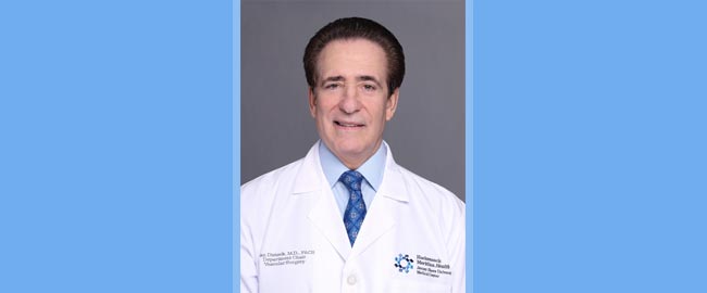 Man with short brown hair wearing a blue shirt with blue tie and a doctors lab coat