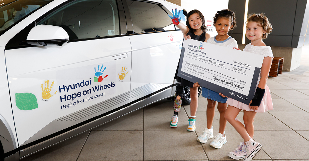 three kids with a large check next to a car