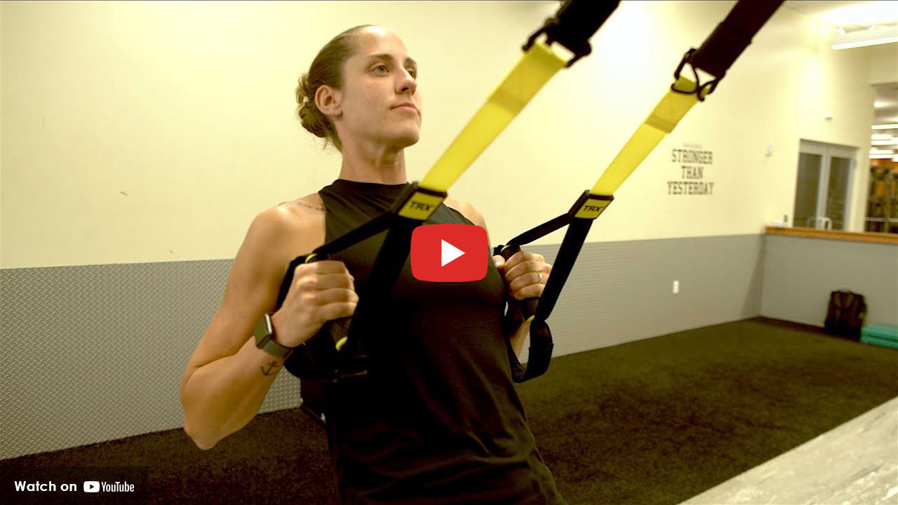Woman performing TRX suspension training exercise in a gym.