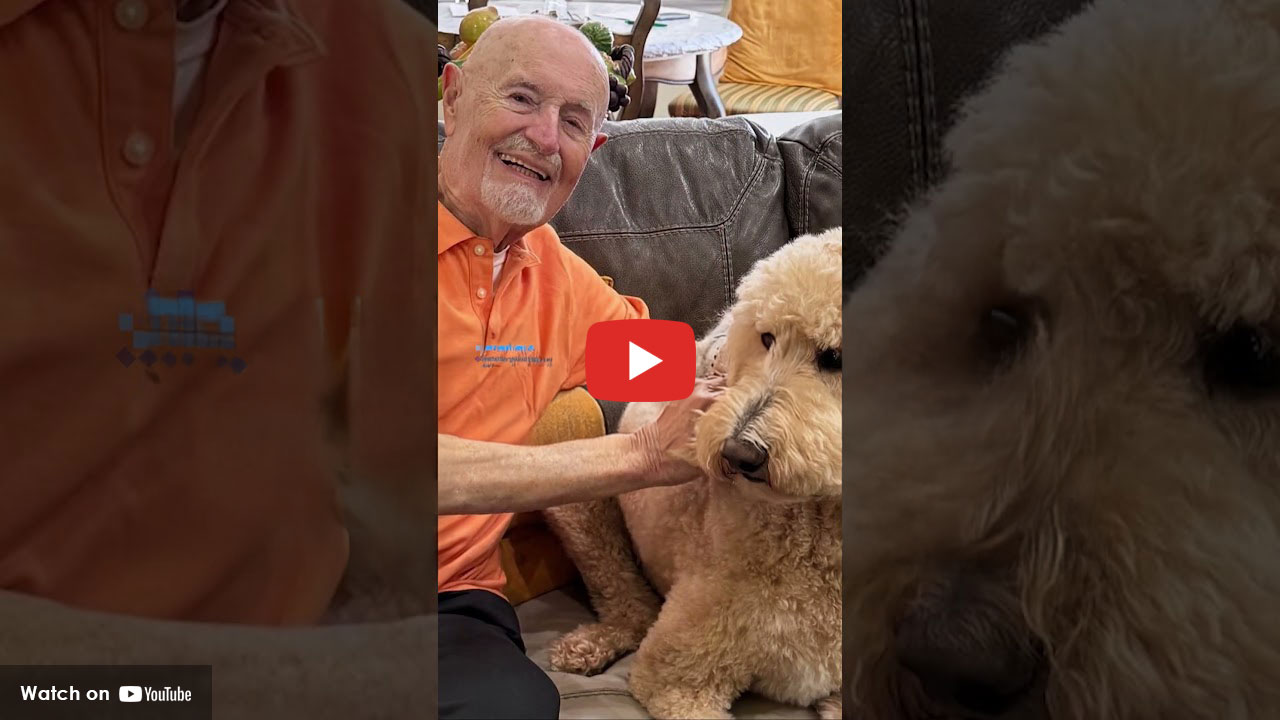 Older man smiling while sitting on a couch and petting a large dog